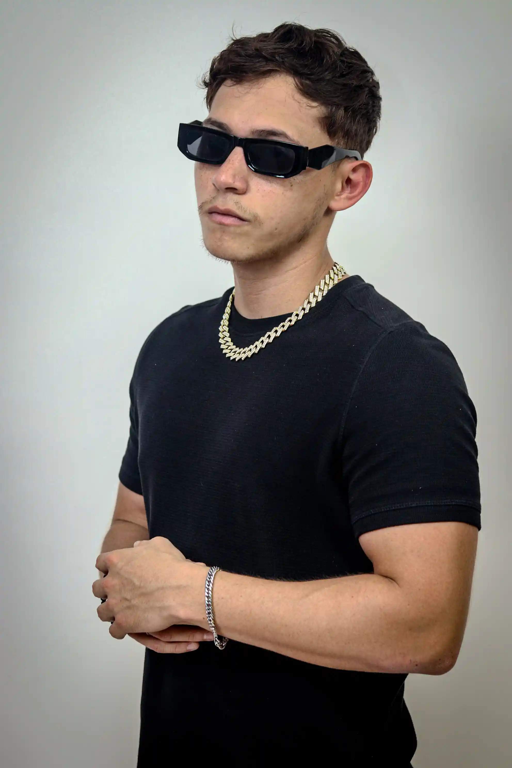 Un retrato de un hombre en una camiseta negra y cadena de oro posa con confianza contra un fondo minimalista