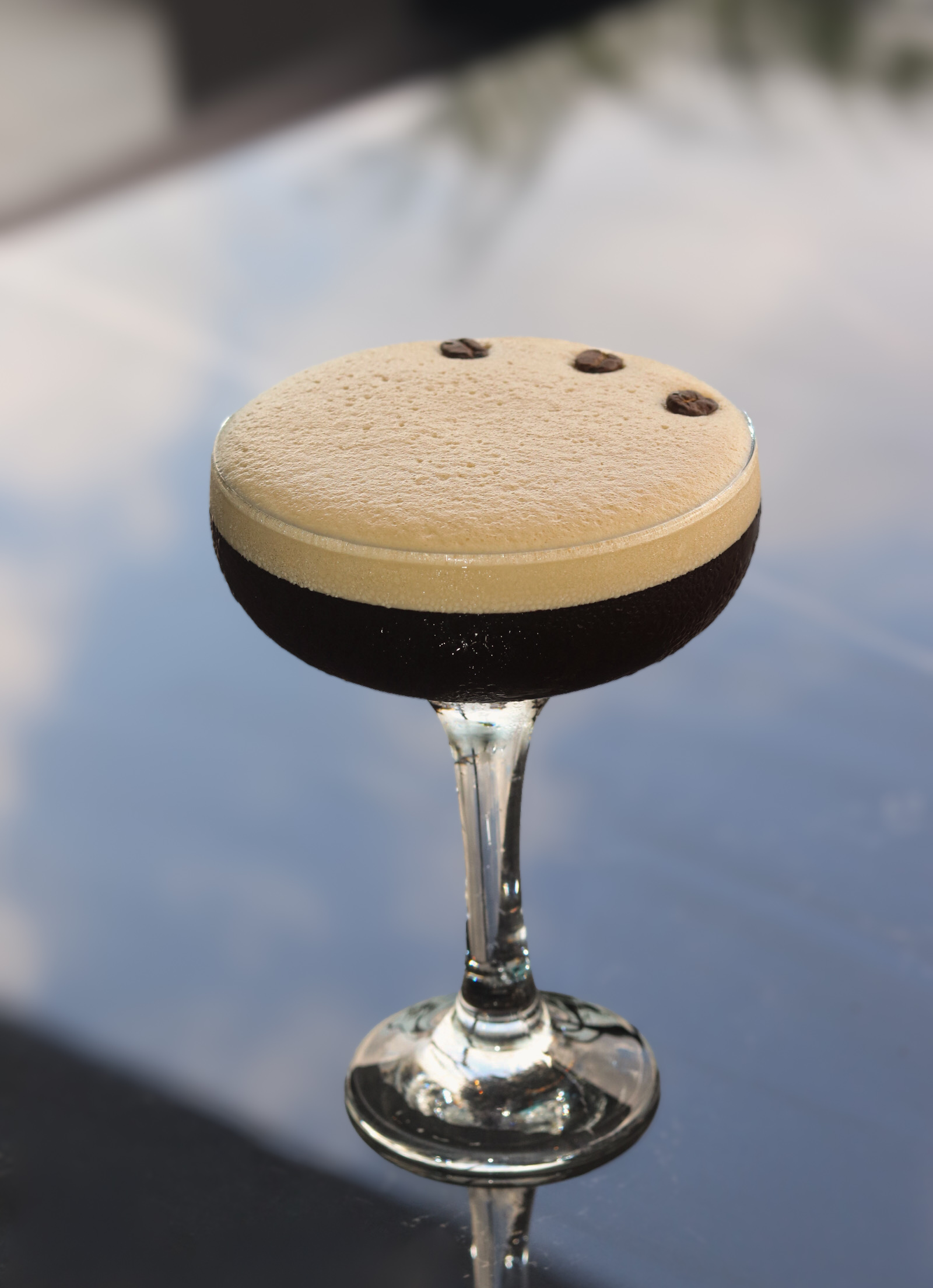 Un rico martini de espresso con espuma cremosa y granos de café, servido en una elegante mesa de cristal
